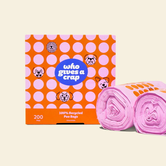 Two rolls and a box of Who Gives a Crap recycled dog poo bags with pink and orange packaging