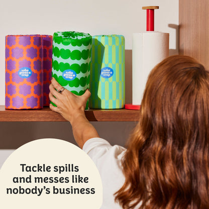 Woman reaches to grab colourful roll of Who Gives a Crap paper towel from kitchen shelf. Sticker on top of image that says ‘tackle spills and messes like nobody’s business’.