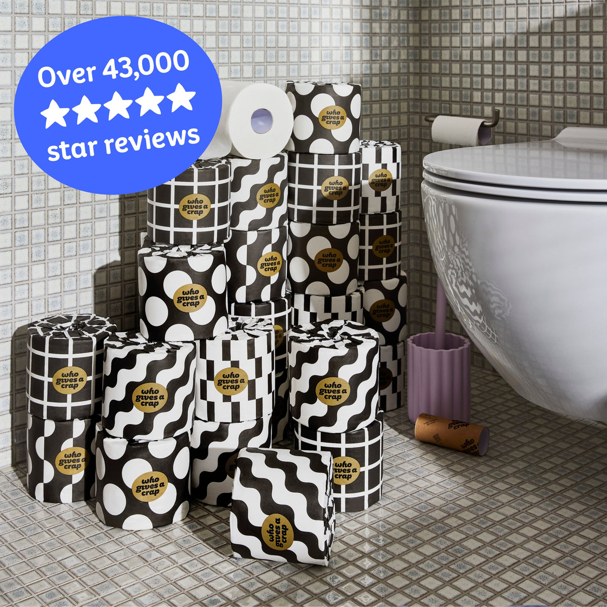 Several rolls of wrapped and unwrapped Premium Toilet Paper sits on the bathroom floor next to a toilet. Copy over the image reads ‘Over 43,000 5 star reviews’.